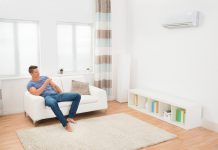 Waarom een airco een meerwaarde is voor je woning jonge man in de woonkamer die airco bedient