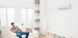 Waarom een airco een meerwaarde is voor je woning jonge man in de woonkamer die airco bedient